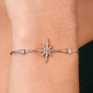 May include: A gold-toned bracelet featuring a starburst design at the center, adorned with small, sparkling crystals. The bracelet has a delicate chain and is accented with additional crystals on either side of the starburst. A piece of jewelry.