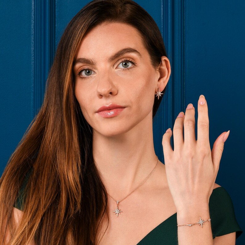 May include: A woman wearing a matching jewelry set. The set includes a necklace, earrings, and bracelet, all featuring a starburst design. The jewelry is a rose gold color and appears to be made of metal and gemstones.