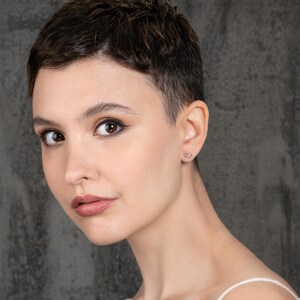 K&ouml;nnte beinhalten: Nahaufnahme einer Person mit kurzen, dunkelbraunen Haaren, die einen kleinen, silbernen Ohrring in Form eines Unendlichkeitszeichens tr&auml;gt.