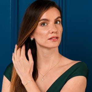 May include: A gold necklace and earrings with a starburst design. The necklace features a pendant with a starburst design and the earrings are small and simple.