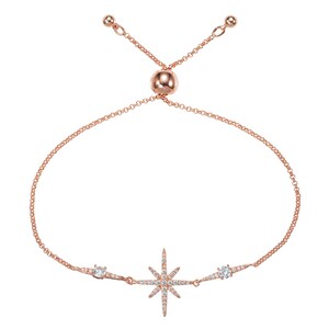 May include: Rose gold-toned bracelet featuring a starburst design with clear, sparkling crystals. The adjustable chain bracelet has a central starburst and two smaller crystal accents.