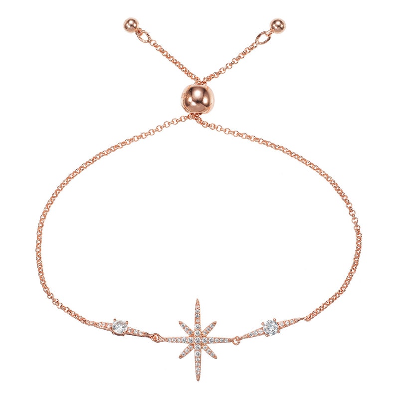 May include: Rose gold-toned bracelet featuring a starburst design with clear, sparkling crystals. The adjustable chain bracelet has a central starburst and two smaller crystal accents.