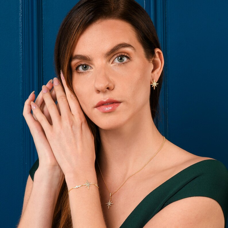 May include: A gold necklace and bracelet set featuring a starburst design with small sparkling stones. The necklace has a pendant and the bracelet has two charms.