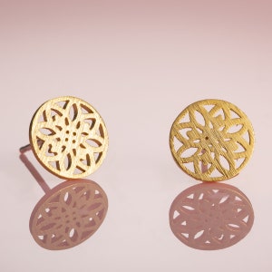 May include: A pair of gold-toned earrings featuring a delicate, intricate floral design. The earrings are round and have a cutout pattern.