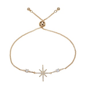 May include: A gold adjustable bracelet with a starburst charm and two smaller round charms, all set with clear cubic zirconia stones.