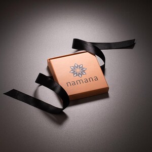 K&ouml;nnte beinhalten: Eine braune Geschenkbox mit einem schwarzen Band darum gebunden. Die Box hat ein wei&szlig;es Logo mit dem Wort "namana" darauf gedruckt.