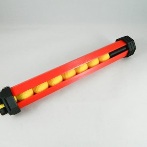 Puede incluir: Una pistola de juguete de plástico roja y negra con un cargador amarillo lleno de pequeñas bolas amarillas.