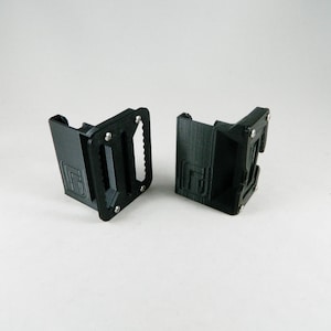 May include: Two black plastic 3D printed clips with a textured surface. The clips have a small metal screw on the side and a small metal loop on the top.