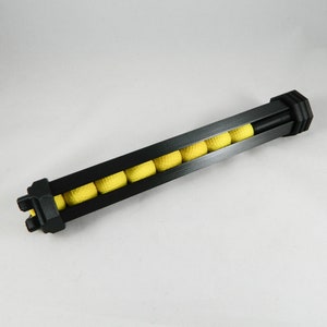 May include: A black plastic magazine with yellow balls inside. The magazine is designed to hold and feed balls into a toy gun.