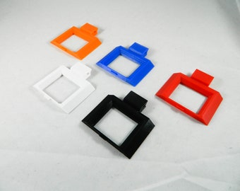Op de afbeelding: Vijf 3D-geprinte plastic frames in verschillende kleuren: oranje, blauw, wit, zwart en rood. De frames zijn allemaal even groot en hebben dezelfde vorm, met een vierkante opening in het midden.