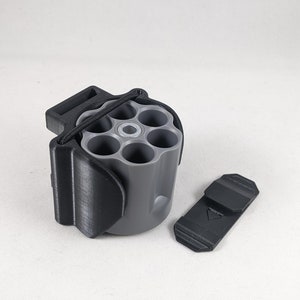 Peut inclure: Un porte-objets en forme de revolver imprimé en 3D noir et gris avec un élastique et un clip noir séparé. Le porte-objets comporte six compartiments pour ranger de petits objets.