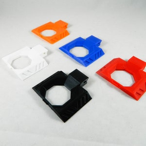 Può includere: Cinque oggetti di forma esagonale stampati in 3D in diversi colori: nero, bianco, rosso, blu e arancione. Ogni oggetto presenta un design in rilievo sulla parte superiore e inferiore.