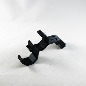 May include: A black plastic 3D printed bracket with three slots. The bracket is curved and has a right angle at the end.