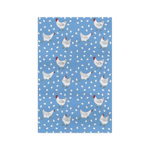 May include: A rectangular, light blue fabric with a repeating pattern of white chickens and white egg shapes. The chickens have red combs and are in various poses. The fabric is likely a kitchen towel or decorative cloth.