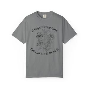 Puede incluir: Una camiseta gris carbón de manga corta con una ilustración botánica de líneas negras en el centro. El texto "if boys will be boys then girls will be girls" está impreso en una fuente negra circular rodeando el gráfico floral.