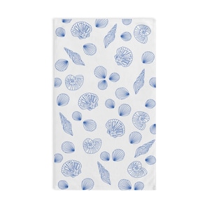 May include: White beach towel with a blue seashell pattern. The towel is covered in a variety of seashells, including clams, scallops, and conch shells.