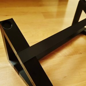 Puede incluir: Estante triangular negro con un agujero en una de las esquinas. El estante est&aacute; hecho de madera y tiene un acabado negro.