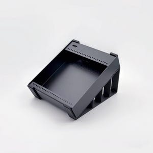 May include: A black, angled storage tray with a rectangular interior and a series of small holes along the top edges. The tray has a minimalist design and is made of a matte black material.