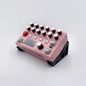 May include: A pink electronic audio device featuring numerous knobs, buttons, and a small screen. The text "EVIL PET" and "ENDORPHINES" are printed on the device. It is supported by a black stand.