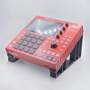 Puede incluir: Un sampler de producción musical Akai MPC One+ rojo con un soporte negro. El sampler tiene una pantalla táctil, 16 pads y varios botones y perillas.