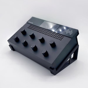 Może przedstawiać: Czarny mikser audio z małym ekranem i sześcioma pokrętłami. Mikser jest oznaczony jako "Impulse" i ma stylizowany symbol fali z przodu.