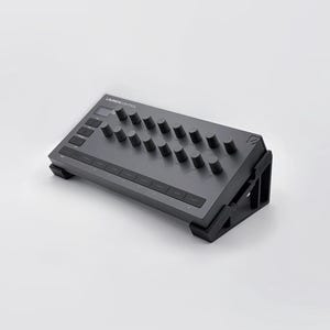 May include: A gray electronic audio controller with multiple knobs and buttons. The device is angled upwards with a black stand. The word "LAUNCHCONTROL" is printed on the top of the device.