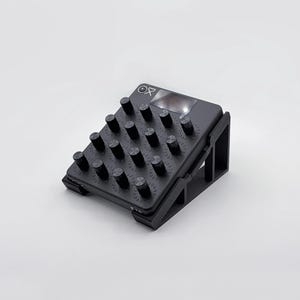 Może przedstawiać: Czarny elektroniczny gadżet z wieloma cylindrycznymi pokrętłami i małym ekranem. Urządzenie jest skierowane w górę i wspierane przez czarny stojak. Powierzchnia ma siatkę małych otworów. Urządzenie ma litery "OP" na górze.