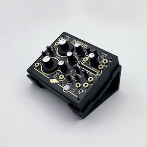 May include: Black electronic synthesizer module with gold accents and the word "INSTRUC" printed on the top. It features numerous knobs, buttons, and input/output jacks. The module is mounted on a black stand.