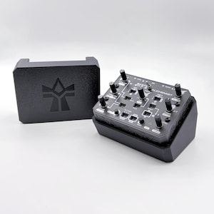 May include: Black electronic device with knobs and buttons, labeled "Earth Alchemist". Includes a matching black box with a logo. The device appears to be a synthesizer or audio processing unit, designed for music production or sound design.