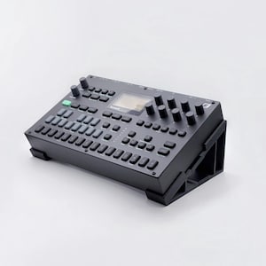 May include: A black electronic music production device with numerous buttons, knobs, and a small screen. The device is angled upwards on a black stand. The overall design is sleek and modern, suitable for studio or live performance.