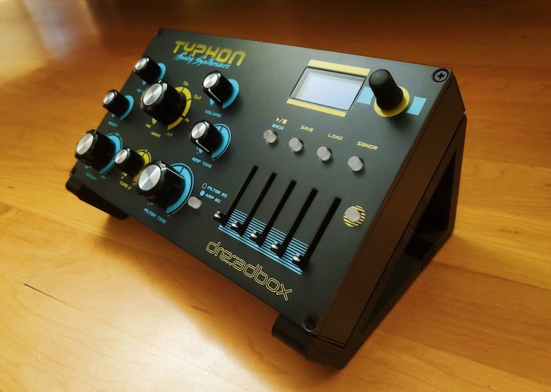 Puede incluir: Un sintetizador anal&oacute;gico Dreadbox Typhon negro con un dise&ntilde;o azul y amarillo. Tiene una peque&ntilde;a pantalla LCD, botones y deslizadores.