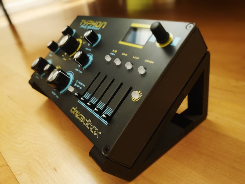 Puede incluir: Sintetizador negro y azul con el texto "TYPHON" y "Dreadbox" en la parte delantera. El sintetizador tiene perillas, botones y deslizadores. Est&aacute; sentado en un soporte negro.