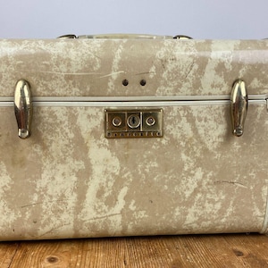 Pode incluir: Uma mala de toucador rígida retangular da Samsonite com um padrão marmoreado em creme e bege. A mala inclui fechos de metal em tom dourado, um mecanismo de fecho central dourado com a marca e uma pega superior para transporte.