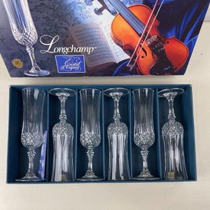 May include: A set of six clear crystal champagne flutes in a blue box. The flutes have a diamond-cut pattern on the lower half of the glass. The box has a picture of a violin and sheet music.
