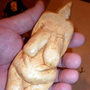 以下が含まれることがあります： 丸いお腹をした裸の女性の彫刻。彫刻は薄い茶色の木でできており、滑らかで磨かれた仕上げになっています。