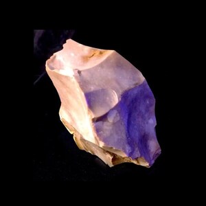 May include: A purple and white flint stone with a rough, irregular shape.
