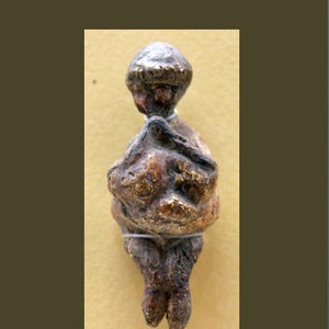 Peut inclure: Une petite figurine en céramique brune représentant une personne à la tête ronde et au corps stylisé. La figurine est assise, les jambes croisées et les bras croisés.