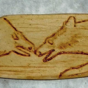 Peut inclure: Une tuile en céramique avec un motif sculpté de deux loups se faisant face. La tuile est de couleur brun clair avec une texture rugueuse.