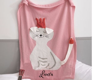 May include: Pink knitted blanket with a white cat wearing a red crown and the name "Laura" embroidered on it.