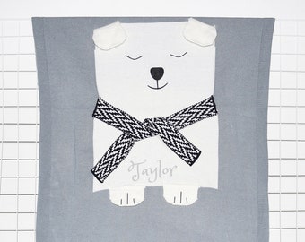 May include: A gray knitted baby blanket with a white polar bear applique. The bear has black eyes, a black nose, and a black and white scarf. The blanket is personalized with the name "Taylor".