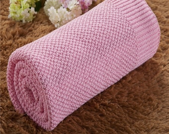 May include: A pink knitted throw blanket with a textured pattern. The blanket is rolled up and is sitting on a brown fuzzy surface.
