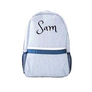 Pode incluir: Mochila listrada azul e branca com o nome "Sam" em escrita preta. A mochila tem um detalhe azul marinho na parte superior e um zíper branco. Bolsos de malha nas laterais.