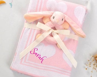 May include: Pink baby blanket with white hearts and a pink bunny rattle with a white ring. The blanket is personalized with the name "Sarah".