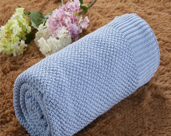 May include: A light blue knitted throw blanket rolled up on a brown fuzzy surface. The blanket has a textured knit pattern.