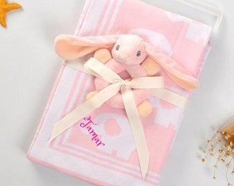 May include: Pink baby blanket with a white border and a white bunny rattle with a pink nose. The blanket is personalized with the name "Tamar" in pink.