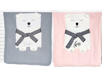 May include: Two knitted baby blankets with polar bear appliques. The blanket on the left is gray with the name "Taylor" embroidered on it. The blanket on the right is pink with the name "Jess" embroidered on it.