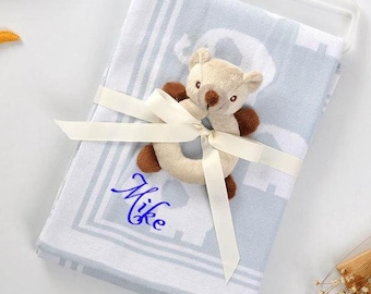 May include: A light blue baby blanket with a white pattern and a plush teddy bear rattle. The blanket is tied with a white ribbon and the name "Mike" is embroidered on it.