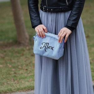 May include: A blue and white striped fabric makeup bag with the name "Alex" embroidered in black.