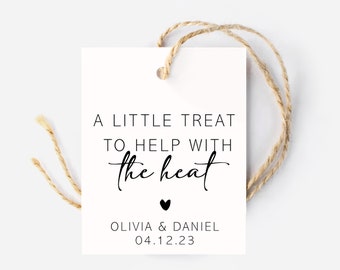 May include: A rectangular white paper gift tag with a hole at the top threaded with natural jute twine. The text reads A LITTLE TREAT TO HELP WITH the heat, followed by a small black heart, OLIVIA & DANIEL, and the date 04.12.23 in black ink.