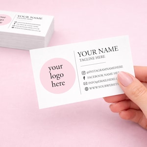 K&ouml;nnte beinhalten: Ein Stapel wei&szlig;er Visitenkarten und eine einzelne Karte mit einem rosa Kreis und dem Text 'your logo here' auf der linken Seite. Rechts stehen 'YOUR NAME', 'TAGLINE HERE' sowie Symbole f&uuml;r Instagram, Facebook, E-Mail und Website.